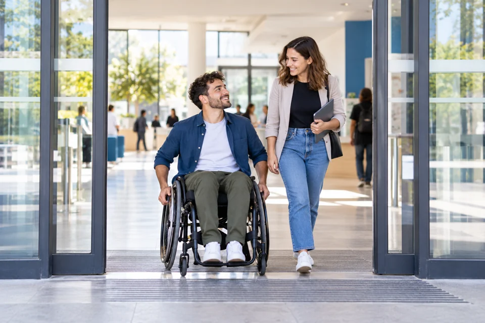 Illustration générée : Une personne en fauteuil roulant et sa collègue dans un bâtiment accessible.